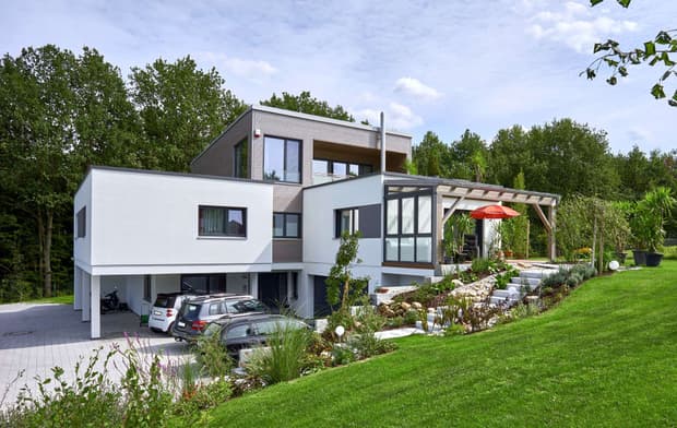 Modernes Holzhaus im Bauhausstil mit drei Gebäudetrakten, zwei davon mit mineralischem Außenputz und Flachdach, einer mit Holzfassade aus Fichtenholzbohlen und Pultdach