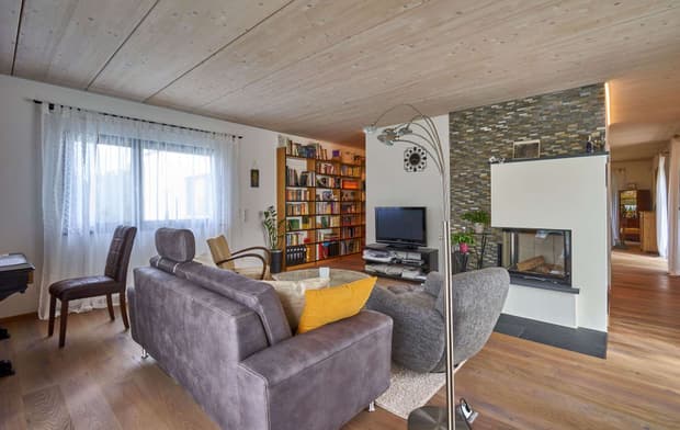 Das Wohnzimmer des modernen Holzhauses im Bauhausstil mit drei Gebäudetrakten, zwei davon mit mineralischem Außenputz und Flachdach, einer mit Holzfassade aus Fichtenholzbohlen und Pultdach