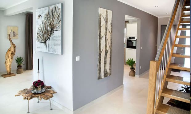 Heller Eingangsbereich im modernen Musterhaus mit Holztreppe, grauen Wänden, Naturdeko, Pflanzen und stilvollen Wandbildern.