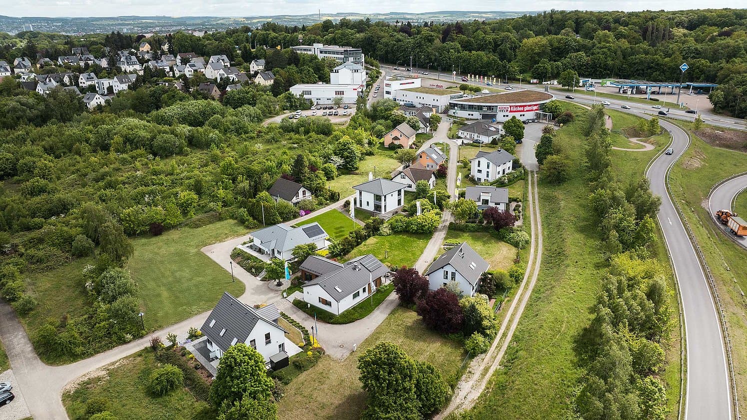 Luftaufnahme kleiner moderner Wohnsiedlung mit Einfamilienhäusern, umgeben von viel Grün und angrenzender Schnellstraße
