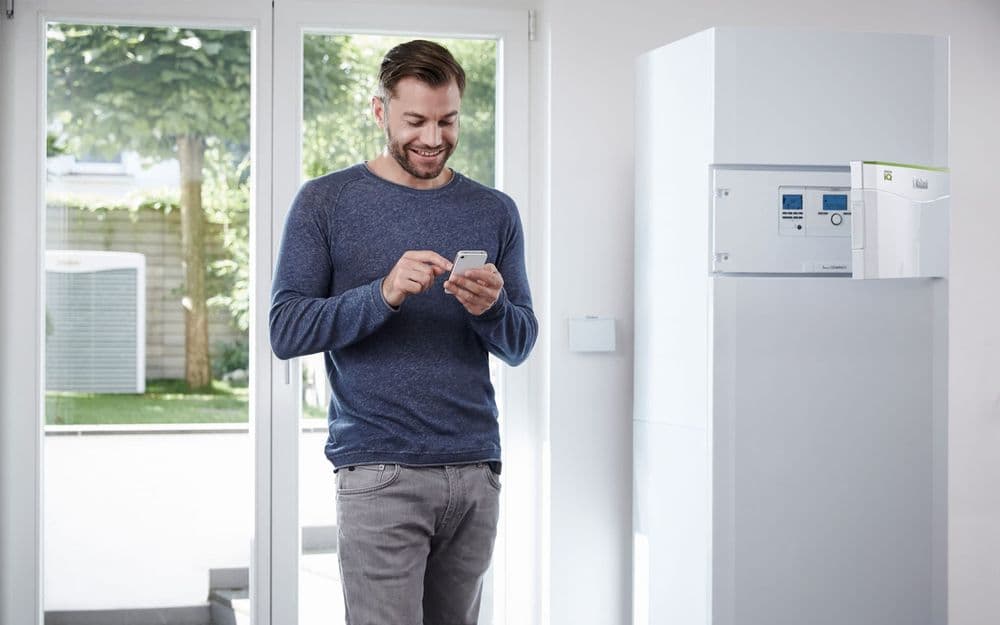 Mann steht in der Küche und guckt auf sein Smart Phone