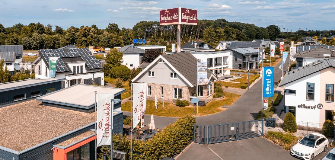 Luftaufnahme einer Mustersiedlung mit modernen Häusern, Fahnen, Straße und großem FertighausWelt-Schild.