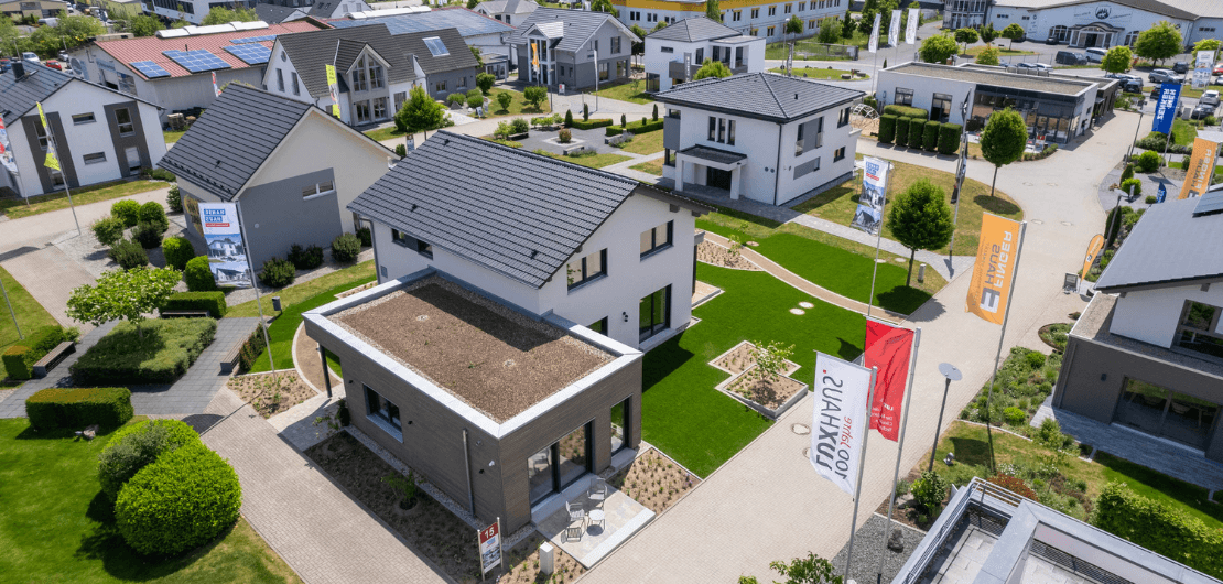 Luftaufnahme einer modernen Mustersiedlung mit Einfamilienhäusern, Wegen, Fahnen und gepflegten Rasenflächen.