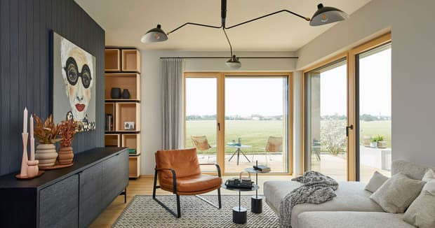 Helles Wohnzimmer im modernen Musterhaus mit Ledersessel, grauem Sofa, Kunst an der Wand und Blick auf Terrasse und Garten.