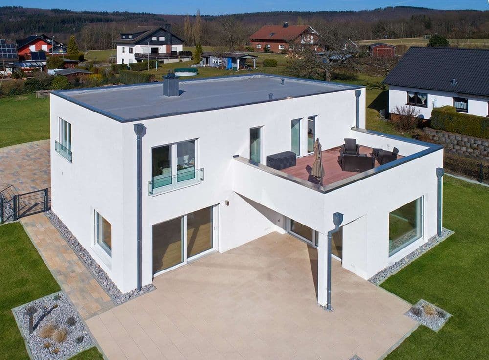 Modernes Flachdachhaus mit Attika, Dachterrasse und großen Fenstern, zeigt klare Linien, minimalistisches Design und energieeffiziente Bauweise.