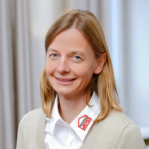 Porträt einer lächelnden Frau mit blondem Haar in weißem Hemd und beige Strickjacke vor hellem Hintergrund