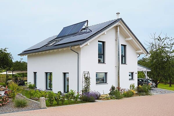 Modernes weißes Einfamilienhaus mit grauem Satteldach und Solarpanelen umgeben von Garten und Straße