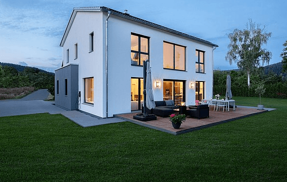 Modernes weißes Einfamilienhaus mit großer Holzterrasse und Garten im Abendlicht
