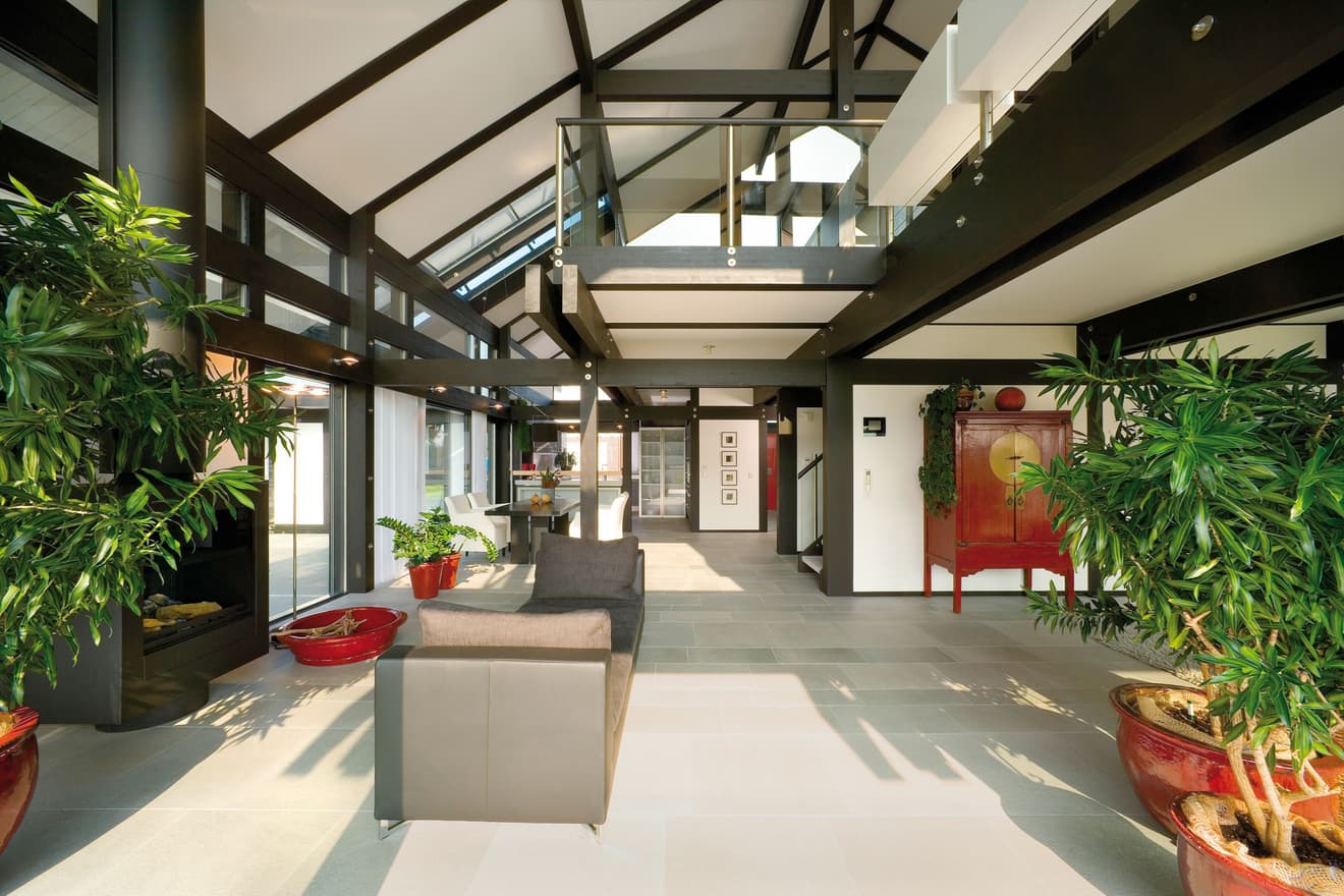 Heller offener Wohnbereich mit Glasfront, schwarzen Stahlträgern, modernen Möbeln und großen Pflanzen, zeigt stilvolles Interieur und Loft-Architektur.