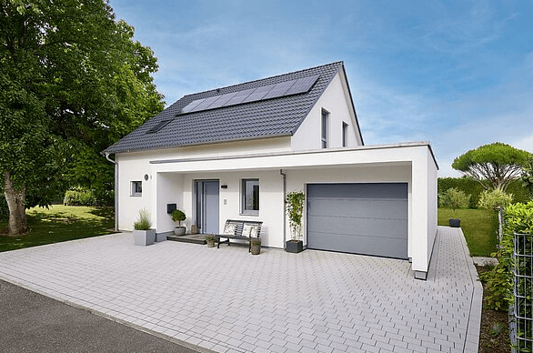 Modernes Einfamilienhaus mit weißer Fassade, grauem Garagentor, Solarpaneelen und großem gepflastertem Auffahrtsbereich