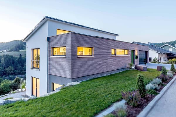 Modernes Architektenhaus mit Holzfassade, großen Fenstern und Hanglage, kombiniert Design, Licht und Natur.