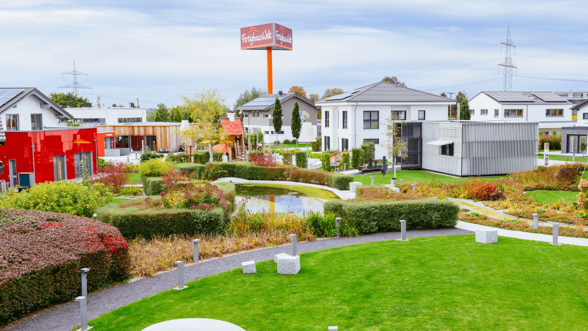 Musterhauspark mit modernen Fertighäusern, Teich und Landschaftsgarten unter bewölktem Herbsthimmel.