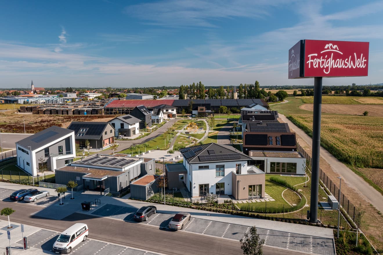 Hausausstellung mit modernen Musterhäusern in Schwarzwald, Solardächern, Parkplätzen und grüner Umgebung bei sonnigem Wetter.