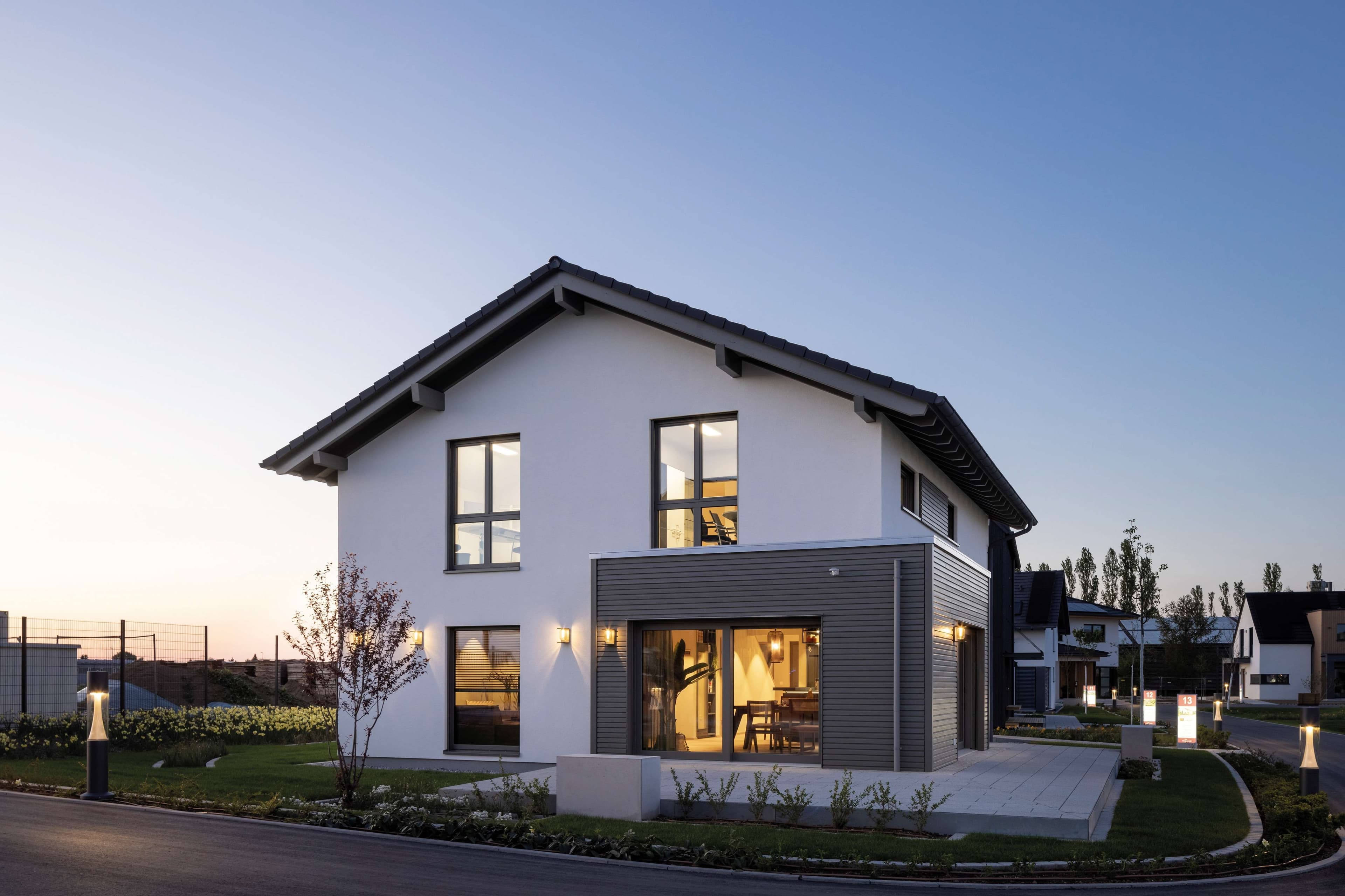 Modernes Einfamilienhaus mit Satteldach, großen Fenstern und Garten bei Sonnenuntergang, zeigt energieeffizientes Wohnen und zeitgemäße Architektur.