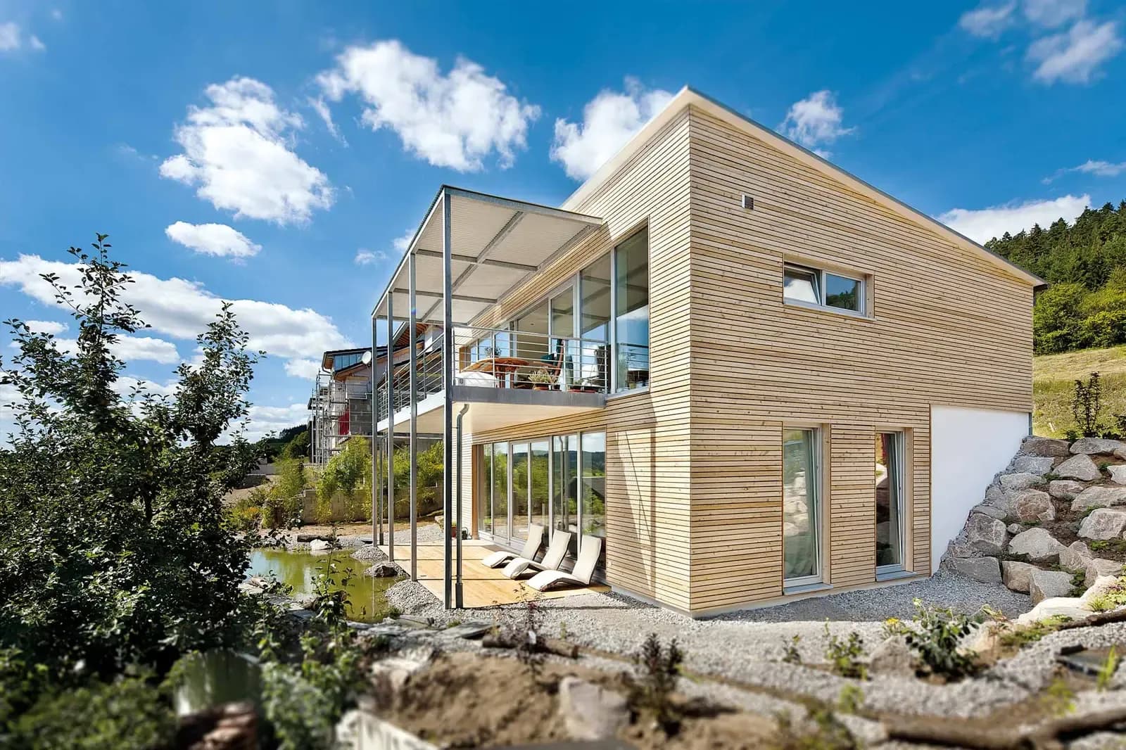 Modernes Holzhaus mit großzügiger Terrasse und natürlichem Schwimmteich. Entdecke nachhaltiges Wohnen in moderner Architektur – perfekt integriert in die Natur.