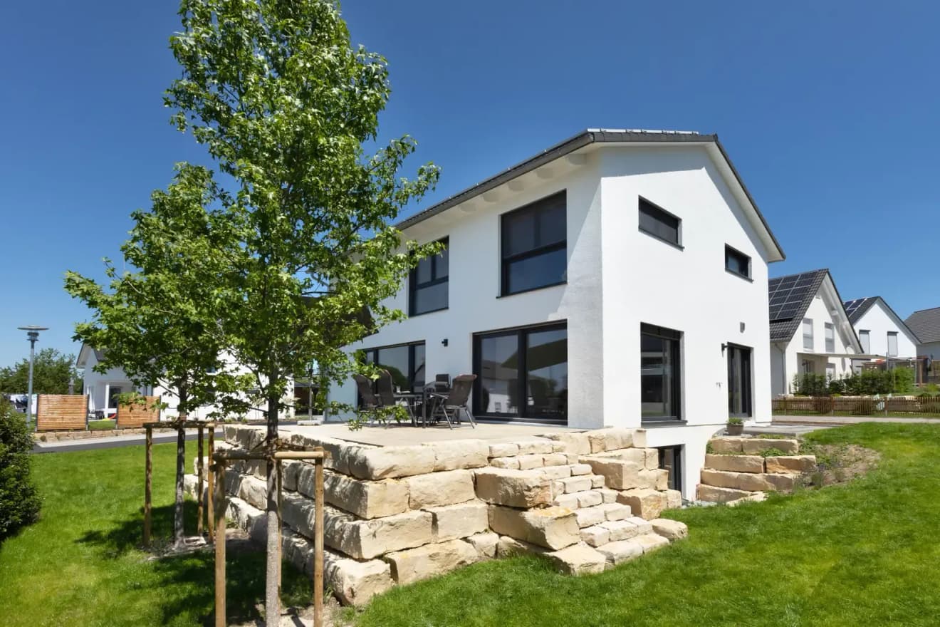 Modernes Einfamilienhaus mit Satteldach und zwei Vollgeschossen – weißes Eigenheim mit großen Fenstern und Natursteinmauer. Inspiration für zeitgemäßen Hausbau.