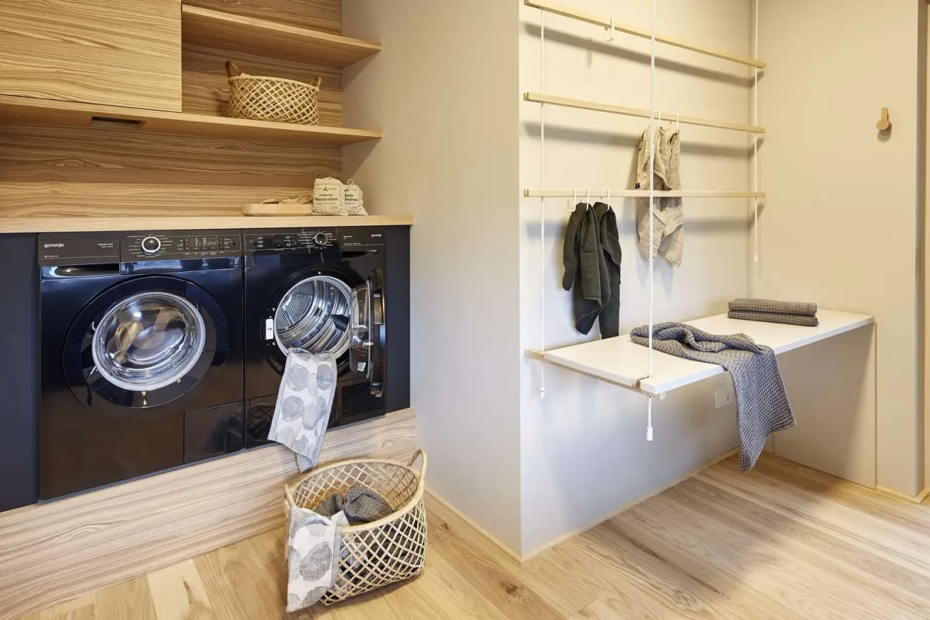 Moderner Hauswirtschaftsraum mit schwarzer Waschmaschine und Trockner, Holzregalen und Aufbewahrung. Praktische Einrichtungsideen für die Waschküche im Eigenheim.