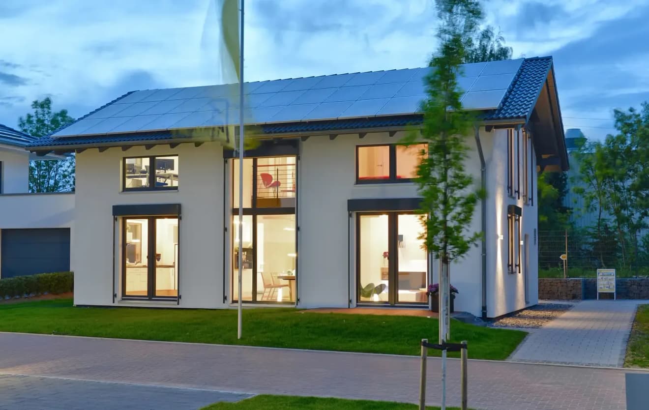 Modernes zweistöckiges Passivhaus mit großer Fensterfront, energieeffizienter Bauweise und Solaranlage auf dem Dach bei Abenddämmerung