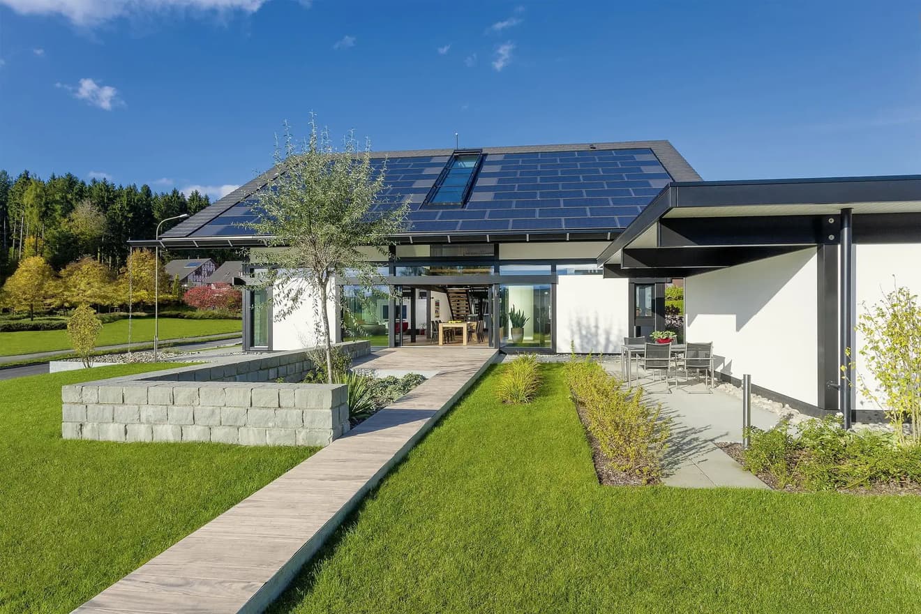 Modernes Plusenergiehaus mit großflächigen Solarpanels auf dem Dach, energieeffizienter Architektur, großen Glasfronten und gepflegtem Garten in sonniger Umgebung