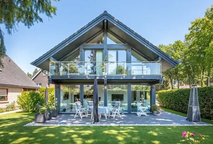 Modernes Einfamilienhaus mit großer Glasfassade, Balkon und sonniger Terrasse – stilvolle Architektur mit lichtdurchfluteten Wohnräumen und gepflegtem Garten.