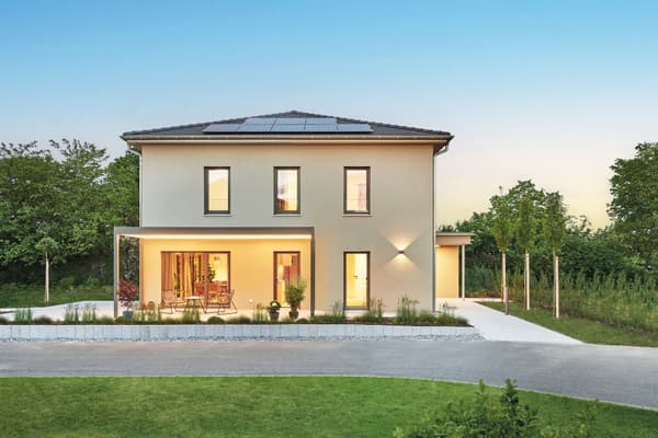 Zweigeschossiges modernes Einfamilienhaus mit Walmdach und Solarpaneelen, hellbeiger Putzfassade, überdachter Terrasse mit Sitzmöbeln und großen Fenstern.