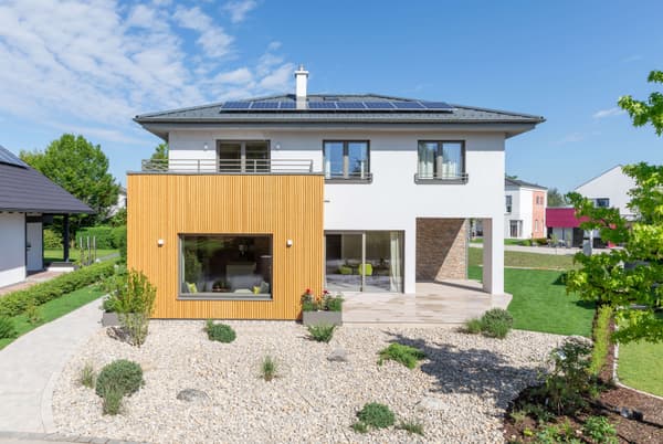 Modernes zweigeschossiges Einfamilienhaus mit Flachdach und Solarpaneelen, kombiniert aus weiß verputztem Obergeschoss und einem erdgeschossigen Anbau mit vertikaler Holzverkleidung.