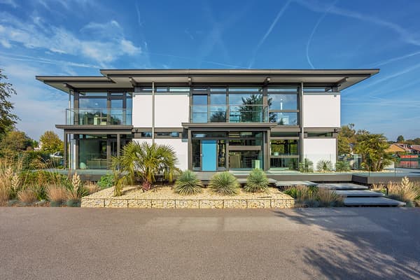 Modernes zweigeschossiges Flachdachhaus mit großflächigen Glasfassaden, weißen Wandpaneelen und grauen Stahlrahmen.