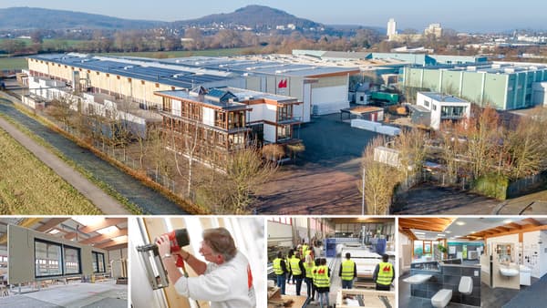 Luftaufnahme eines großen Fertighaus-Werksgeländes mit mehreren Hallen, Verwaltungsgebäuden und Parkflächen, umgeben von Feldern und Hügeln im Hintergrund.