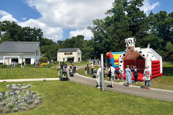 Familienveranstaltung im Musterhauspark bei sonnigem Wetter; im Vordergrund eine aufblasbare Hüpfburg in Form eines Dalmatiners, umgeben von spielenden Kindern und Erwachsenen mit Kinderwagen