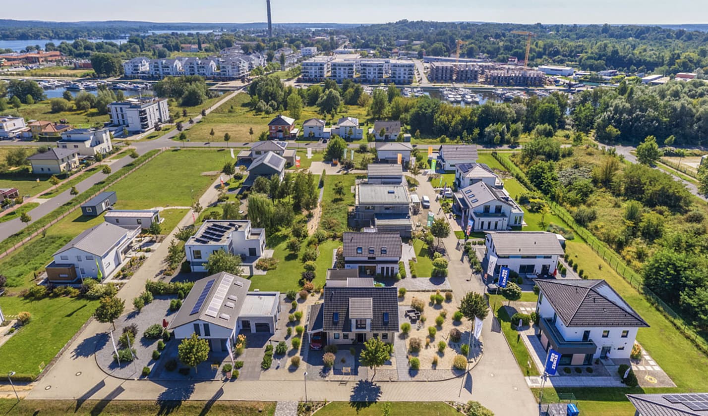 Luftaufnahme moderner Einfamilienhäuser mit Gärten und Solarzellen in einer grünen Vorstadtlandschaft bei Sonnenschein