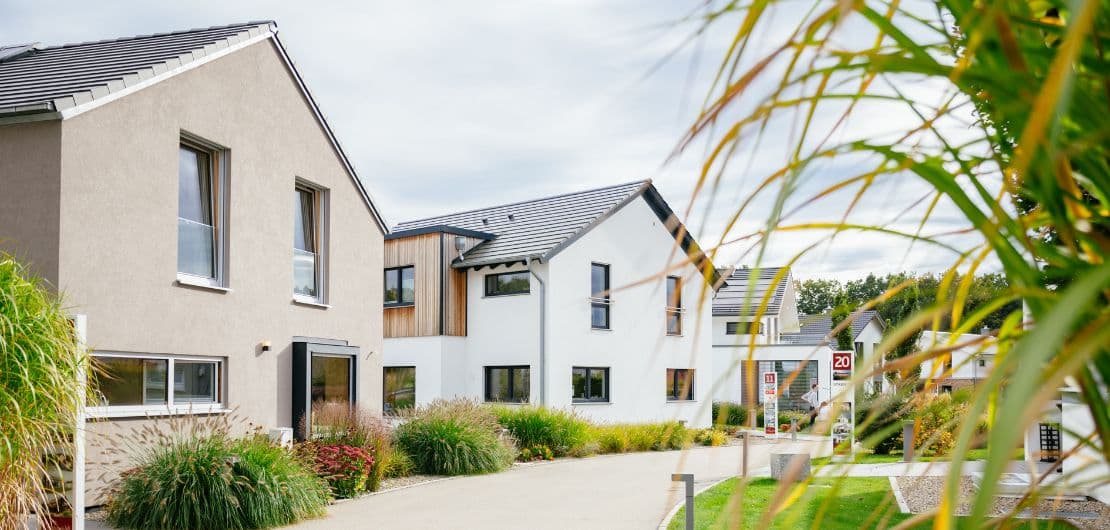 Moderne Reihenhäuser mit hellen Fassaden, Ziergräsern und gepflastertem Weg unter bewölktem Himmel