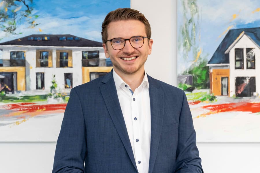 Dunkelhaariger Mann im Anzug lächelt freundlich in die Kamera.